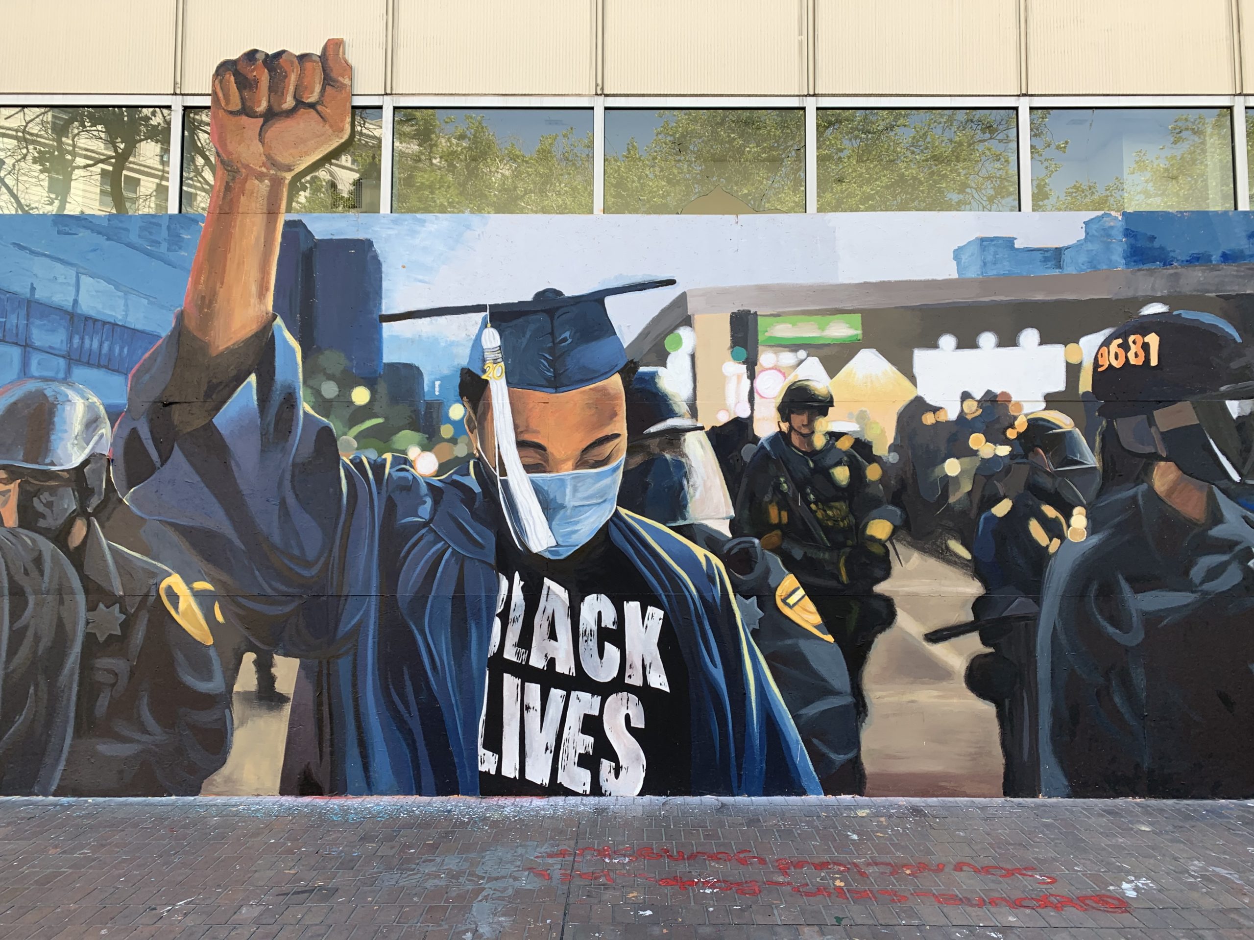 Mural with a young black man in a cap and gown with fist up surrounded by police in military gear.