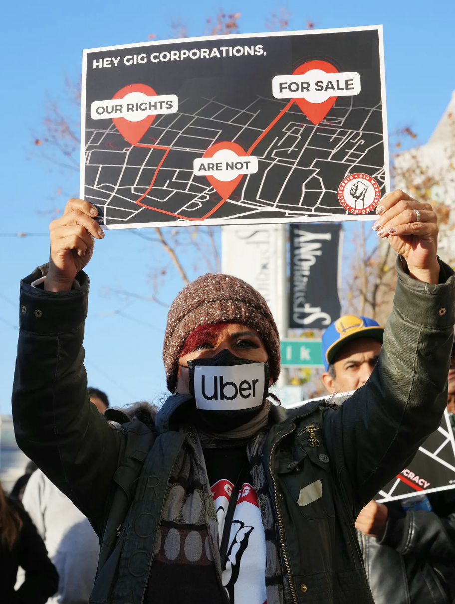 Protestor with Uber mask holding up a sign that says, "Hey, gig corporations, our rights are not for sale."